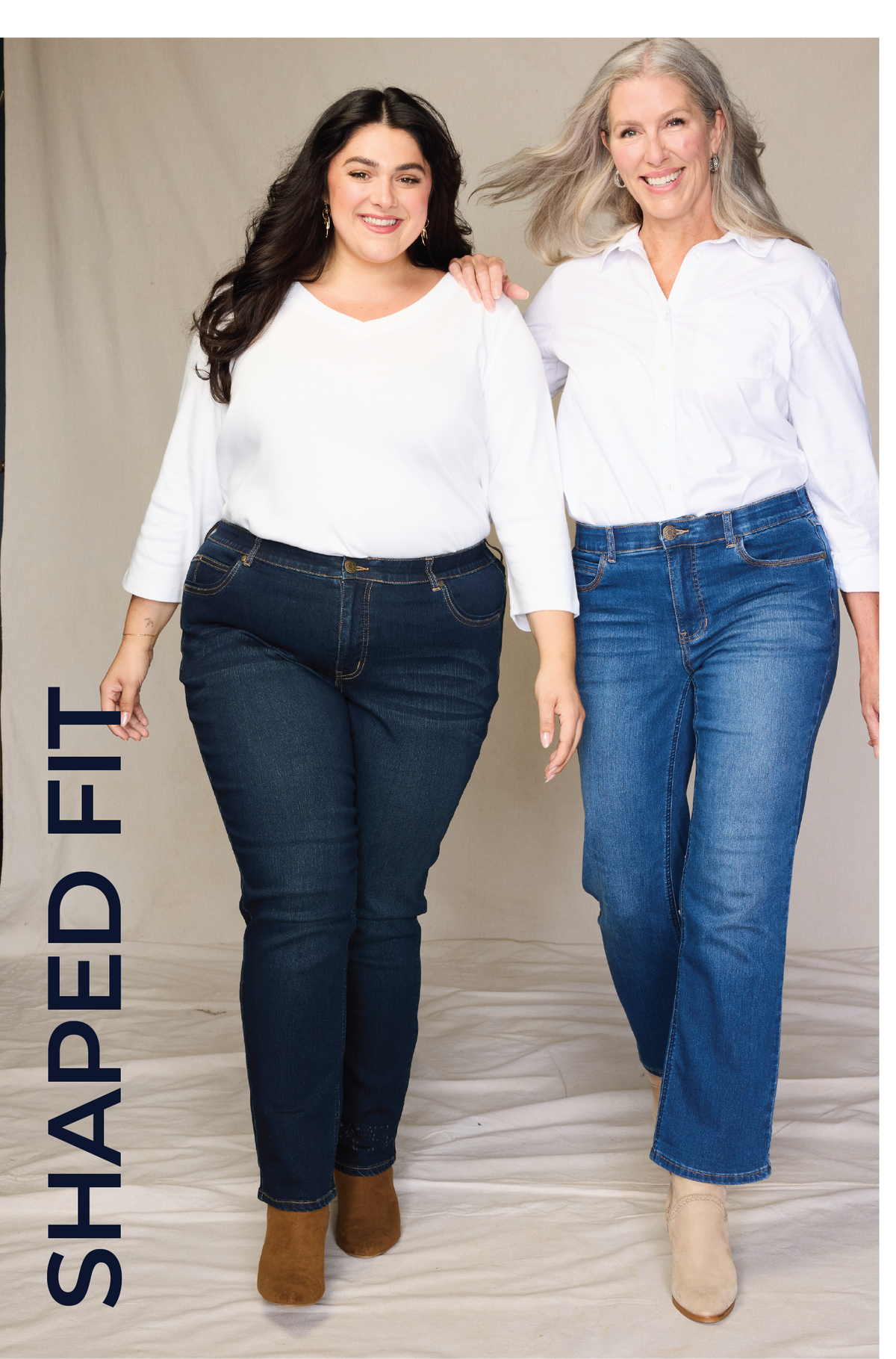 Two women modeling fitted blue jeans against a neutral studio backdrop, with one woman wearing dark blue jeans and the other wearing lighter blue jeans. A vertical text overlay on the left reads 'SHAPED FIT'.