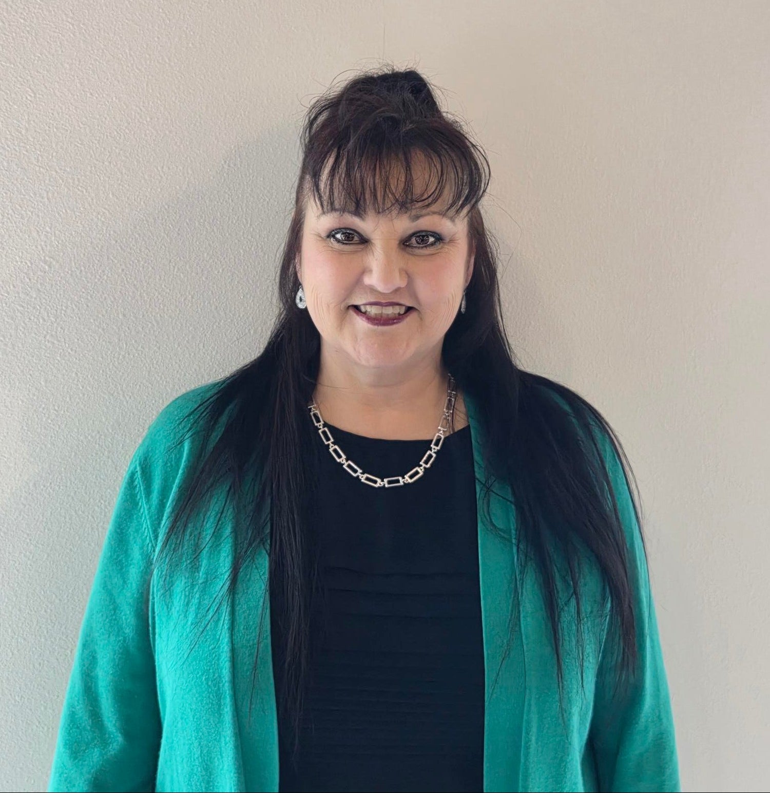Woman wearing a turquoise jacket and black top against a plain background